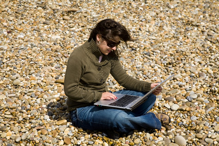在海滩上工作的年轻女子笔记本电脑工作图片