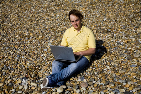 在海滩上工作的年轻人用笔记本电脑工作图片