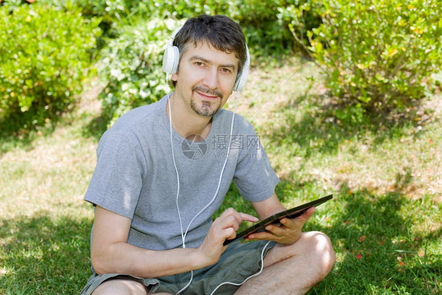 青年男子在户外持有带耳机的平板电脑图片