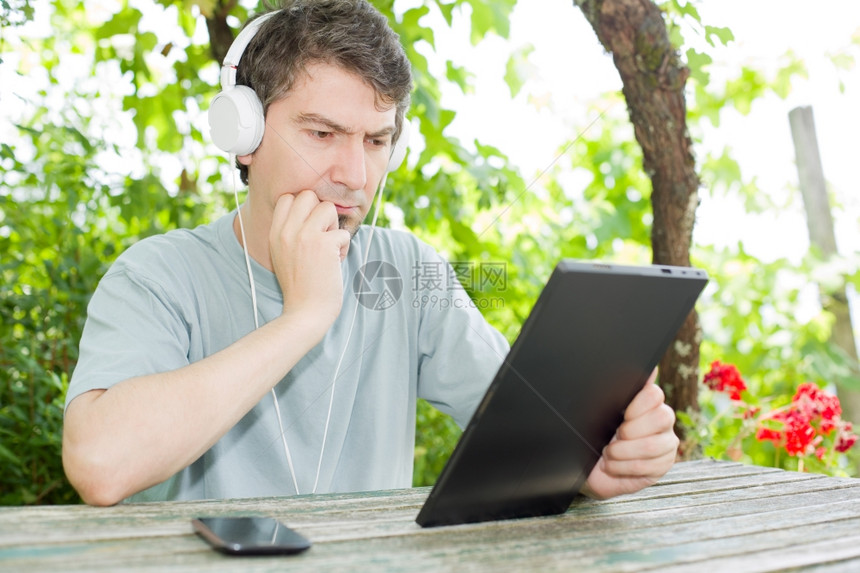 青年男子在户外持有带耳机的平板电脑图片