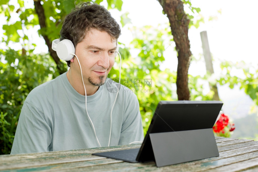 青年男子在户外用耳机平板电脑工作图片