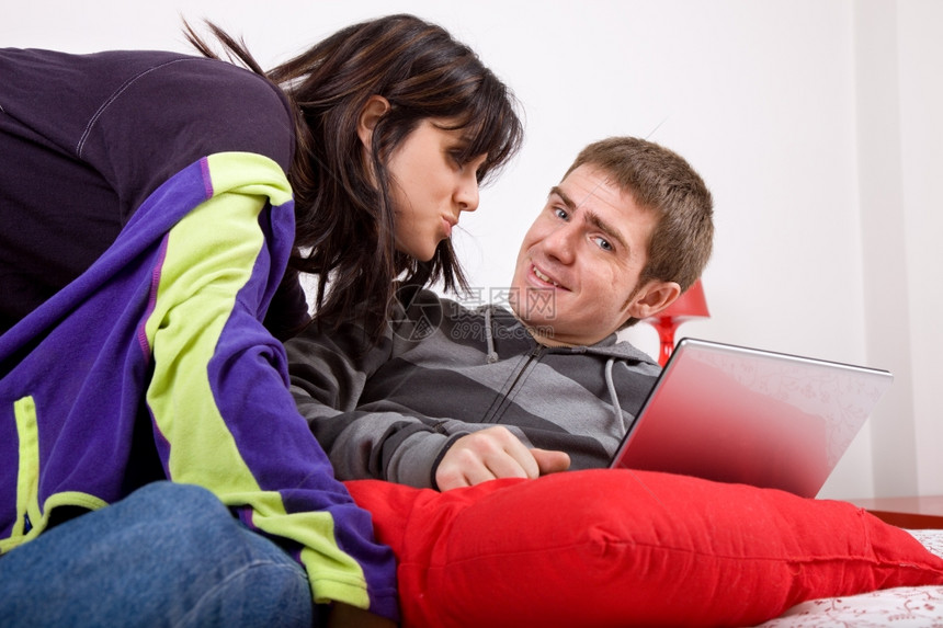 带笔记本电脑在床上的年轻幸福夫妇图片