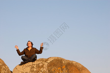 年轻人在岩石上冥想用天空作为背景高清图片