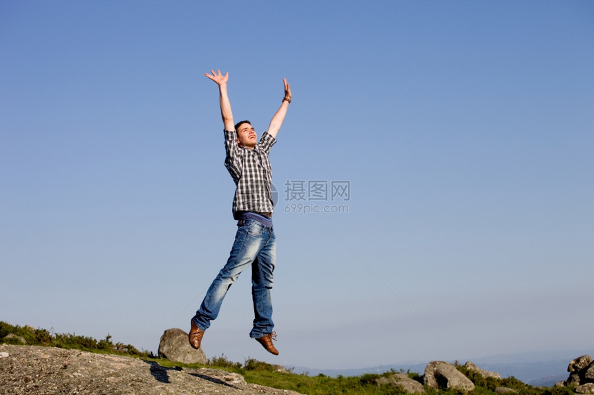 年轻快乐的男孩与一个巨大的跳跃在岩石顶上图片