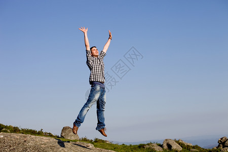 年轻快乐的男孩与一个巨大的跳跃在岩石顶上图片