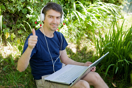 男人坐在草地上用笔记本电脑工作背景图片