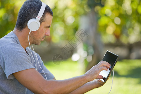 男人用平板电脑放轻松听音乐耳机在公园户外图片