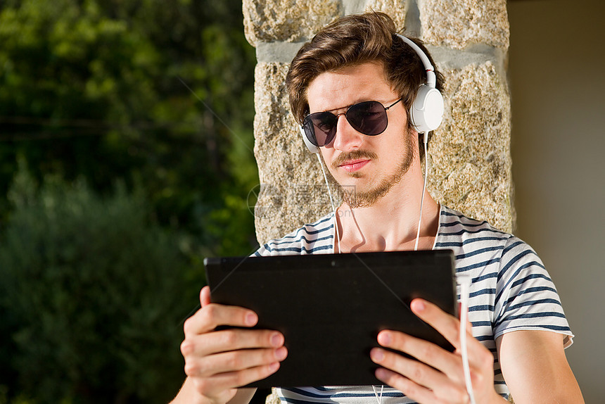 年轻人用平板电脑放松听音乐用耳机户外图片