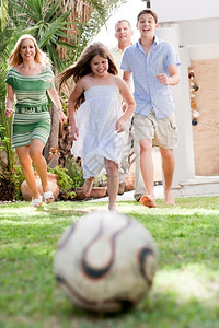 快乐的家庭踢足球奔向家后院的摄像机图片