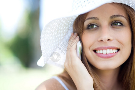 使用手机贴近戴帽子微笑的年轻女士肖像图片