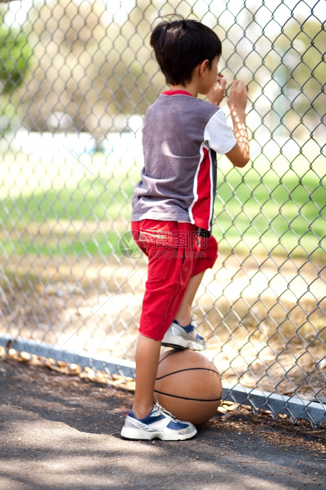 年轻篮球选手的后视镜握着球在腿下透过栅栏看球图片