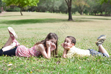可爱的孩子躺在绿草地上看着彼此在公园里图片
