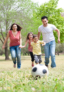 父母和两名幼儿在户外绿色田野踢足球图片