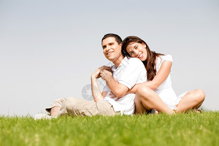 快乐的年轻女带着双臂围她的丈夫肩上躺在公园里图片