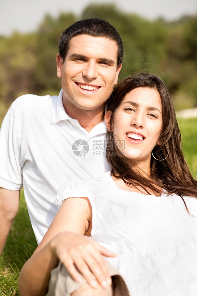 快乐的年轻夫妇肖像坐在公园里笑着坐图片