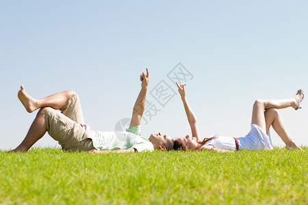 年轻夫妇躺在草地上指向天空在公园户外图片