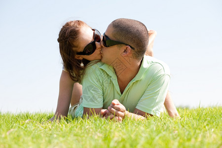 美丽的年轻夫妻躺在草地上亲吻图片