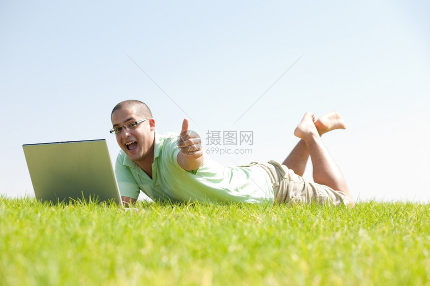 一名青年男子用笔记本电脑坐在公园的草地上图片
