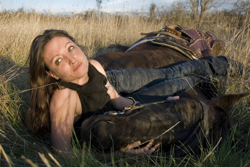 年轻的女子和她黑马躺在田里图片