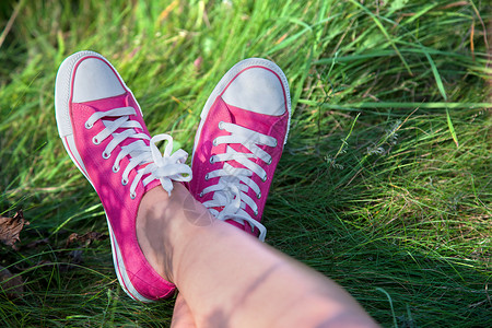 阳光明媚的夏日穿着粉色运动鞋在草地上穿着女孩腿的粉色运动鞋图片
