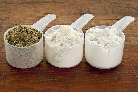 乳清蛋白粉用于测量三种蛋白粉的塑料杯来自左草籽惠油隔热放在石灰木表面背景