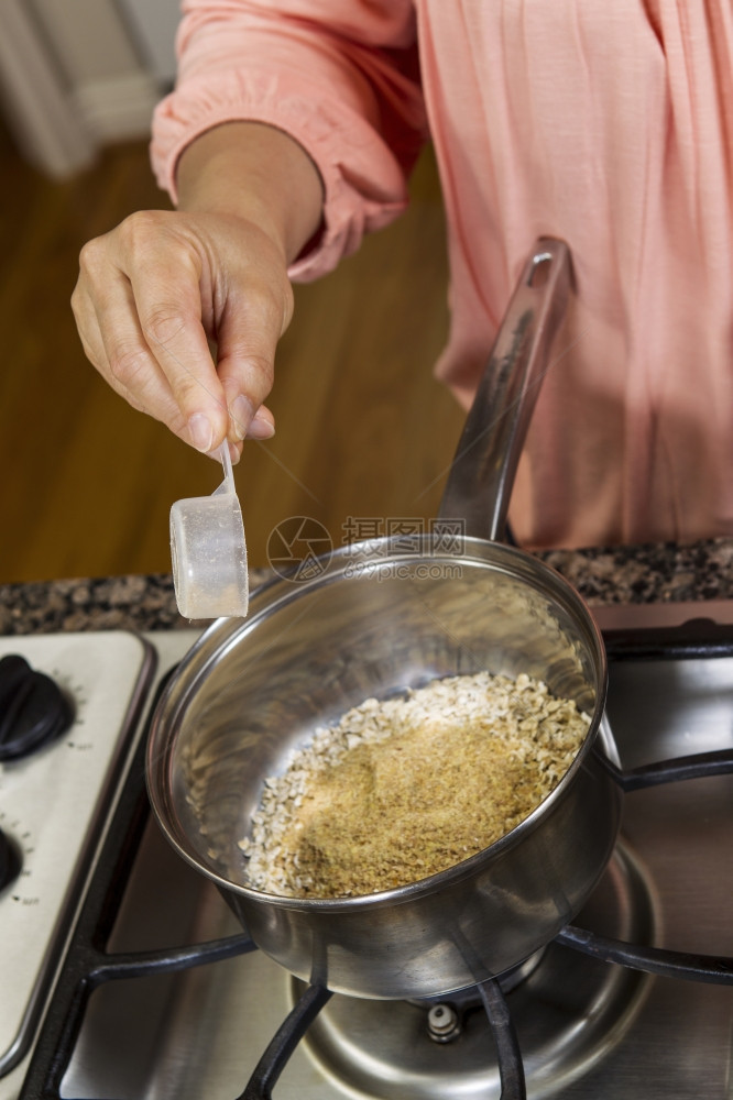 妇女在炉灶顶上做饭时在燕麦早餐中添加小热量图片