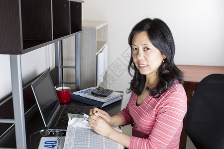 亚洲成年妇女用电脑计算器眼镜和咖啡杯在桌上撕毁税册图片