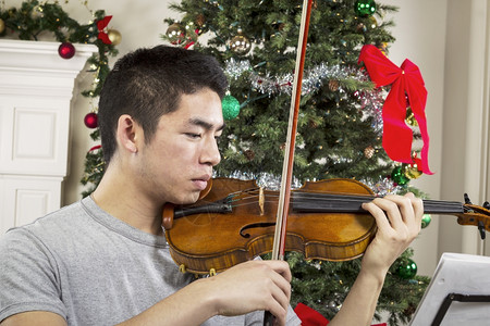 年轻成男子在幕后用圣诞树拉小提琴图片