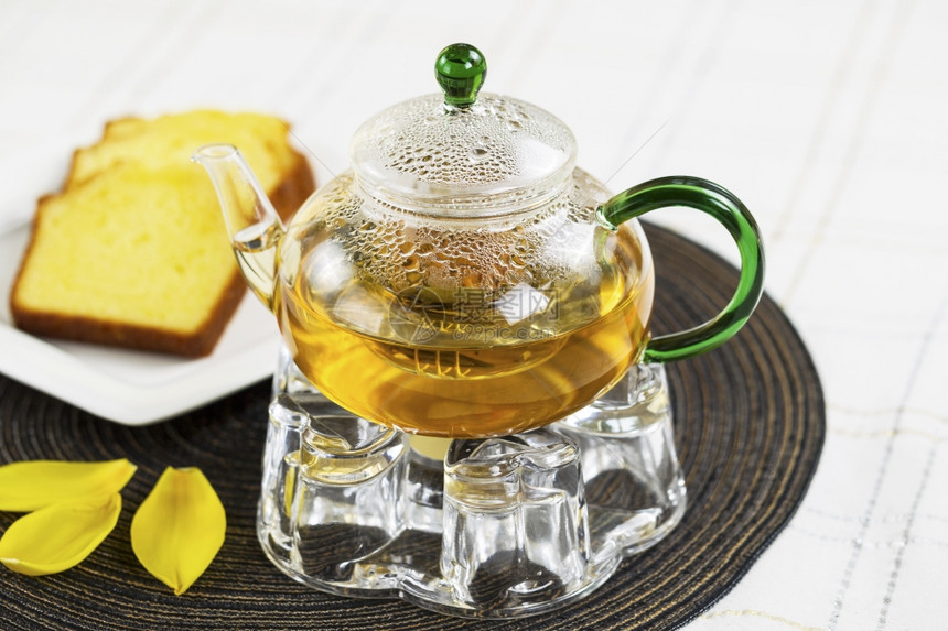 绿色茶壶以为焦点金柠檬饼白色桌布背景的黄叶垫图片