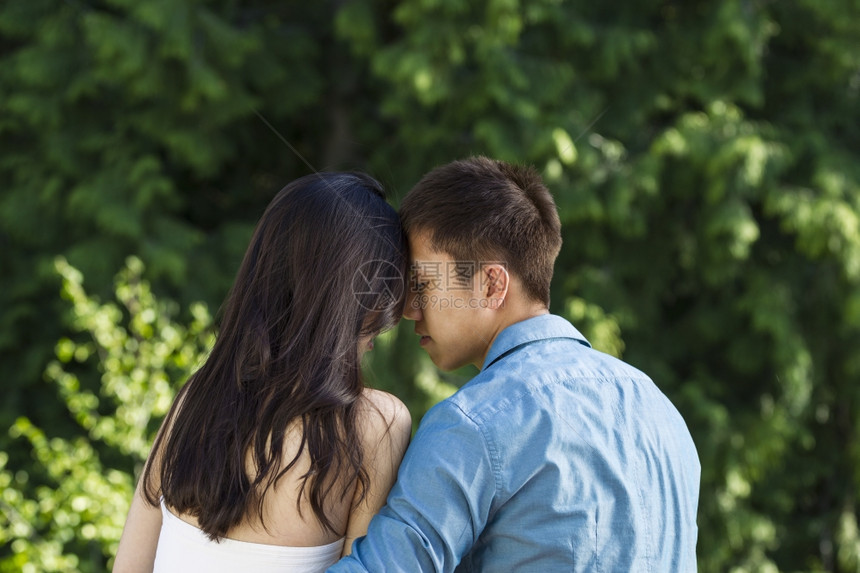 一对年轻成夫妇触摸前额到的横向照片背景有绿树图片