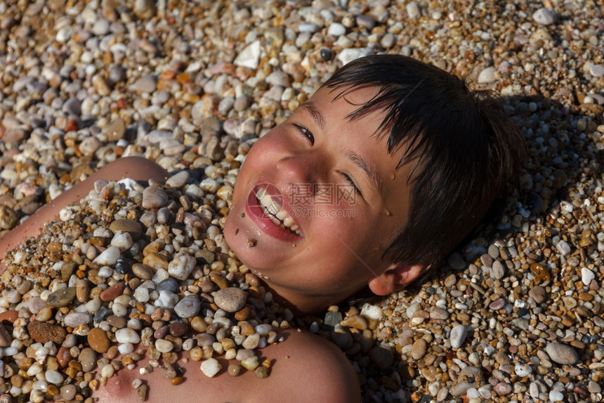 笑的十二岁男孩在海滩上洒满石块图片