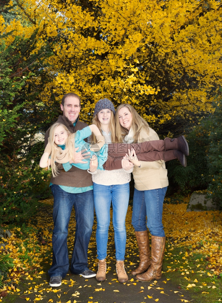 家人在秋天公园散步时抱起最小女儿的垂直照片图片
