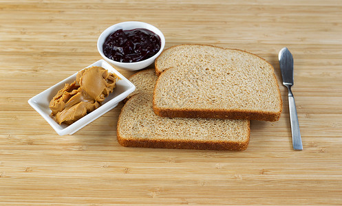 花生酱和果冻三明治成分的横向相照和在下面布满天然竹切板的刀子图片