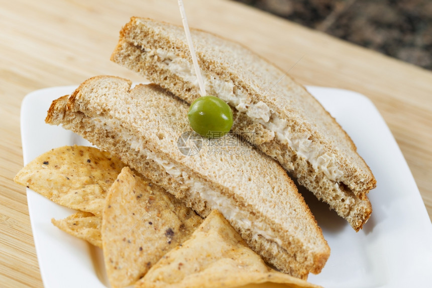 金鱼三明治只绿橄榄和薯片的横向近照其重点是单一绿橄榄和薯片底部有天然竹切削板底部有厨房柜台图片