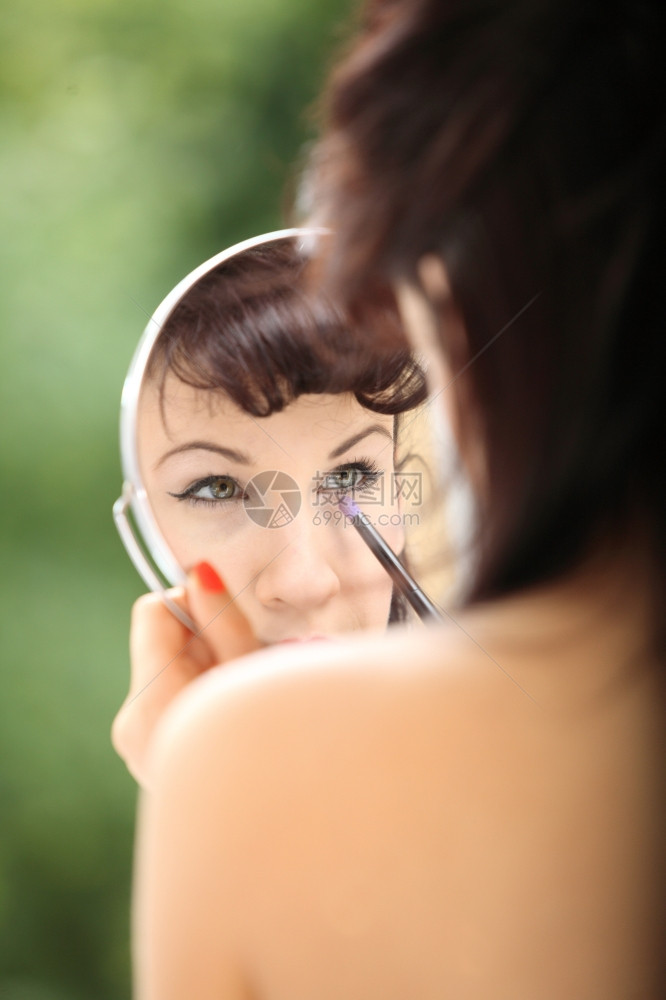 年轻女子准备在室内参加晚会女孩的回化风格用刷子来化妆看着镜子绿色的模糊背景图片