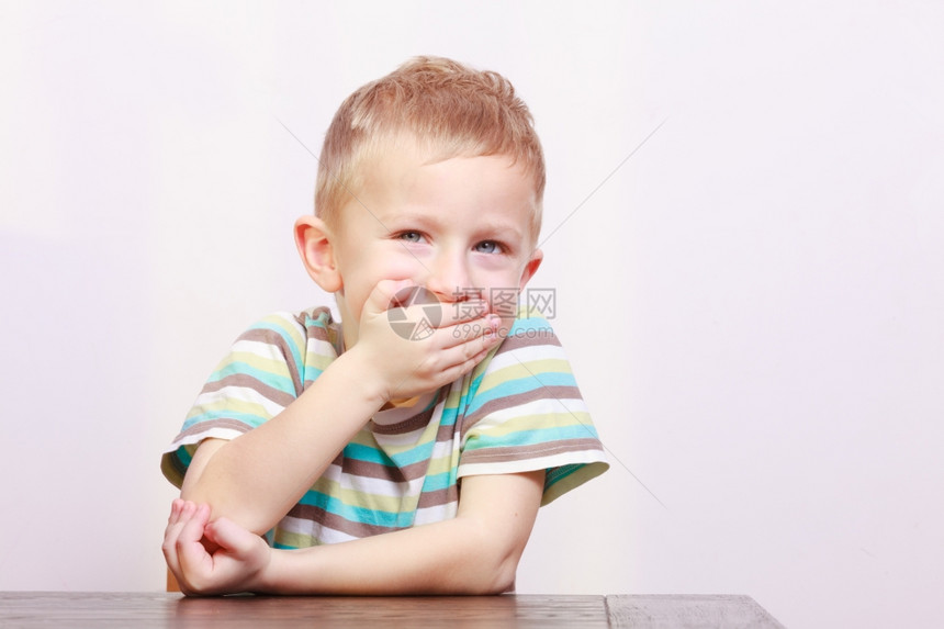金发的男孩子用手在室内桌子上遮住嘴图片