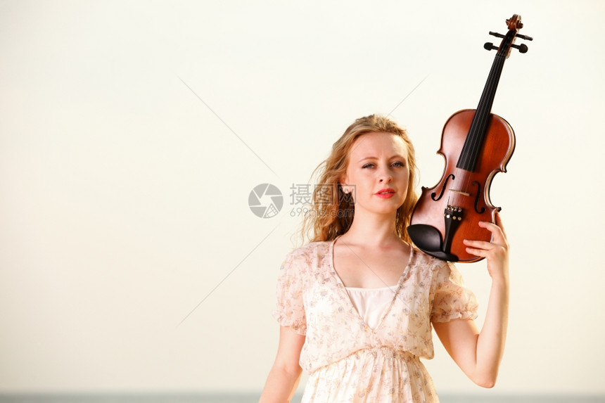 金发女孩在海滩上的音乐情人拿着小提琴喜欢音乐的概念图片