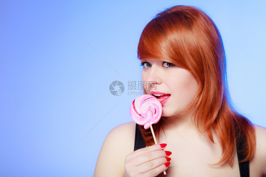 拿着糖果的感年轻女人红头发孩在紫罗兰上吃甜的棒糖图片