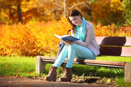 秋天年轻女性坐在公园长凳上读书图片