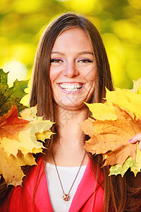 秋天季节笑的年轻女孩肖像在秋天公园森林里拿着丰富多彩的叶子图片