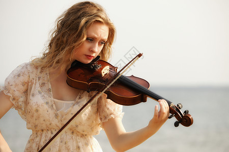 海滩上玩小提琴的金发女音乐情人的肖像爱音乐概念图片