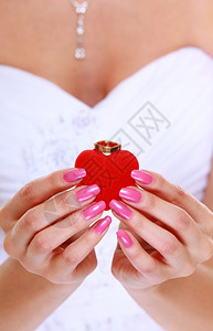 穿白裙子的新娘女手和订婚或结戒指放在红心框里图片