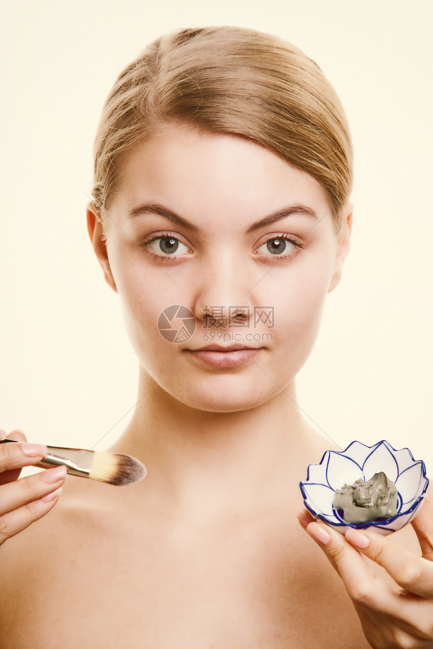 照顾皮肤用刷子在脸上戴粘土面具的年轻女照顾干燥的情谊女孩施虐和美容治疗图片