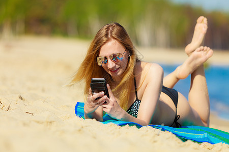 暑假比基尼日光浴的感女孩在海滩晒黑年轻女人在海边用手机放松夏天图片