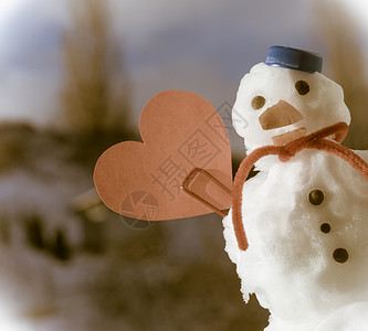 雪心圣诞小雪人穿着蓝螺丝顶的色雪人帽子红围巾和心爱的短片符号牙签在户外冬季节特定情人39日蓝天空背景塞皮亚语调背景