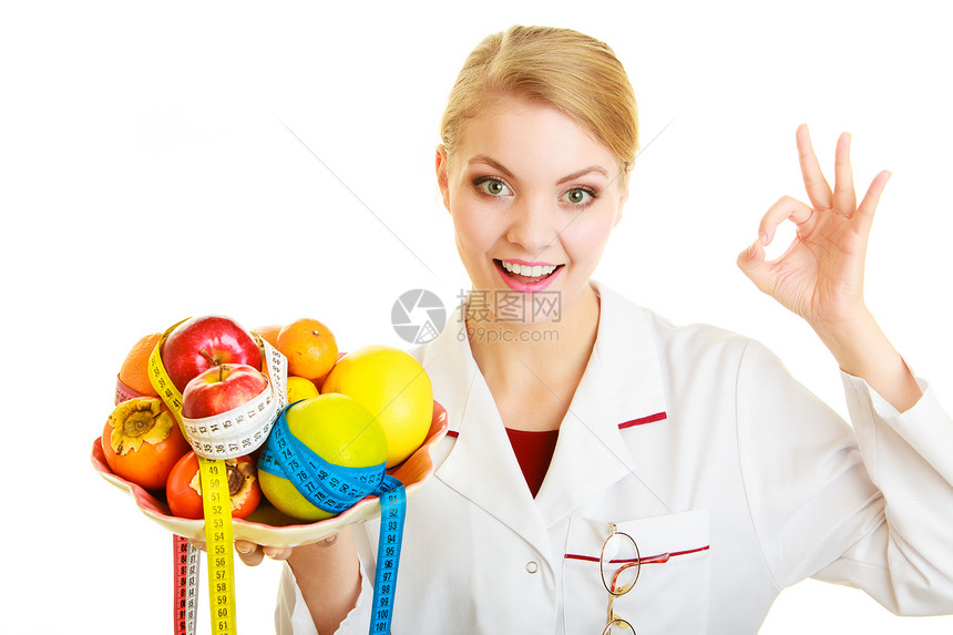 白大衣上的女人拿着水果和多彩度量的磁带被隔离医生建议健康食品显示好的手势饮食图片