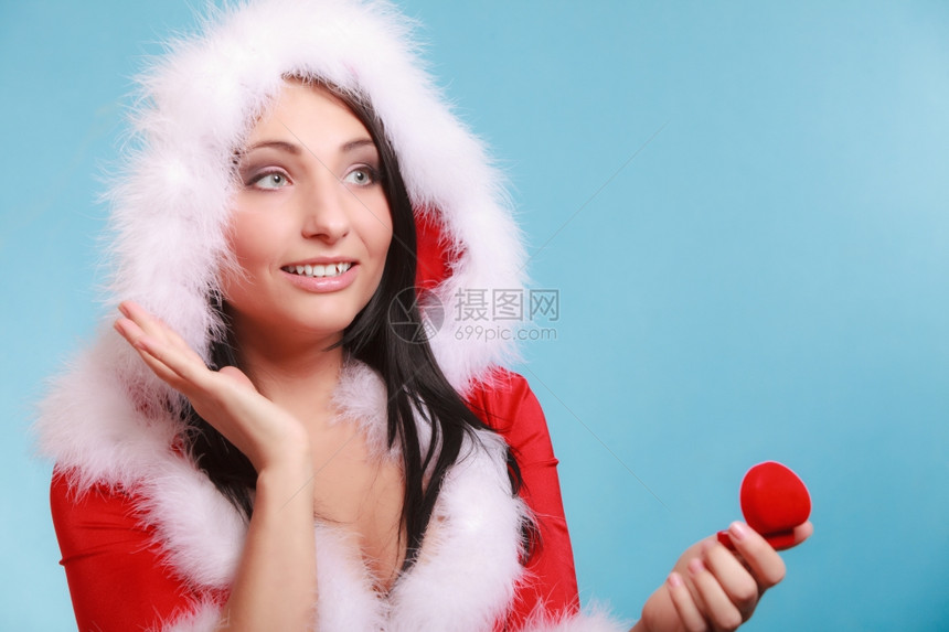 穿着圣达克萨斯服装的快乐年轻女孩开张时红心的礼物盒蓝色背景的订婚戒指圣诞礼物图片