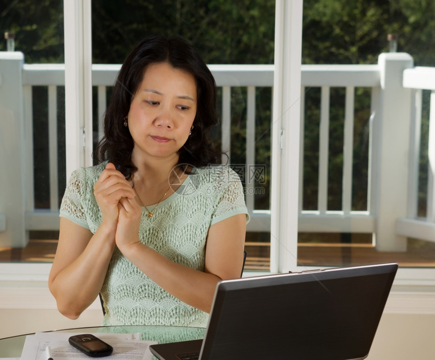 成年妇女在家里工作时用笔记本电脑手机和纸放在桌子顶部和大窗底时观看计算机屏幕的照片图片