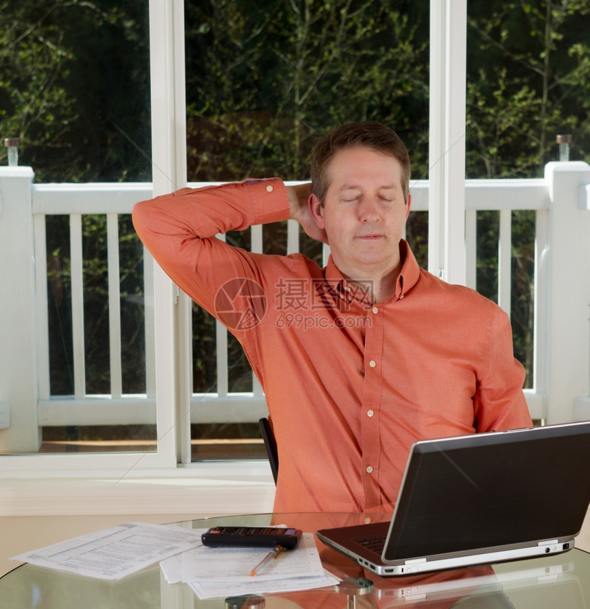 成人男子在家工作时用笔记本电脑计算器和纸在桌子顶部大窗在背景上休息的照片图片