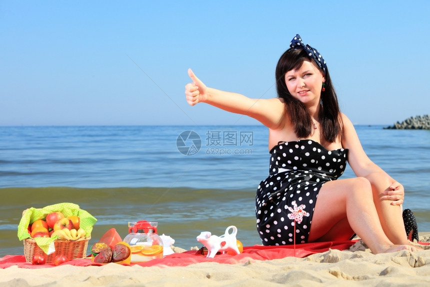 美丽的女人坐在沙滩上的红色毯子图片